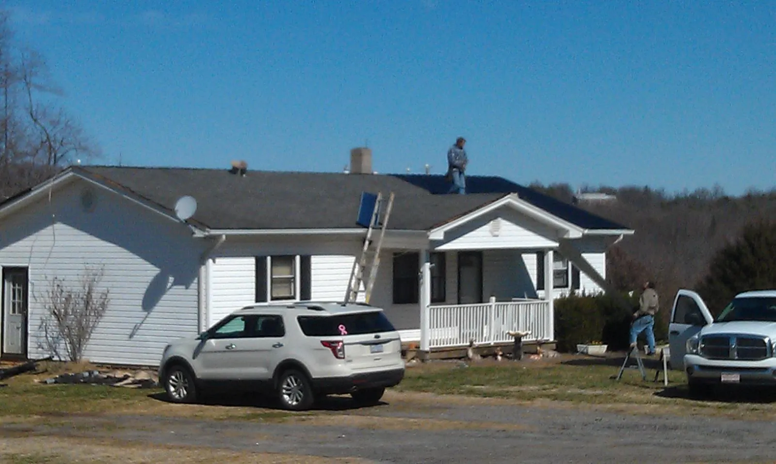 Roofers stripping shingles from a white ranch house roof in Winslow